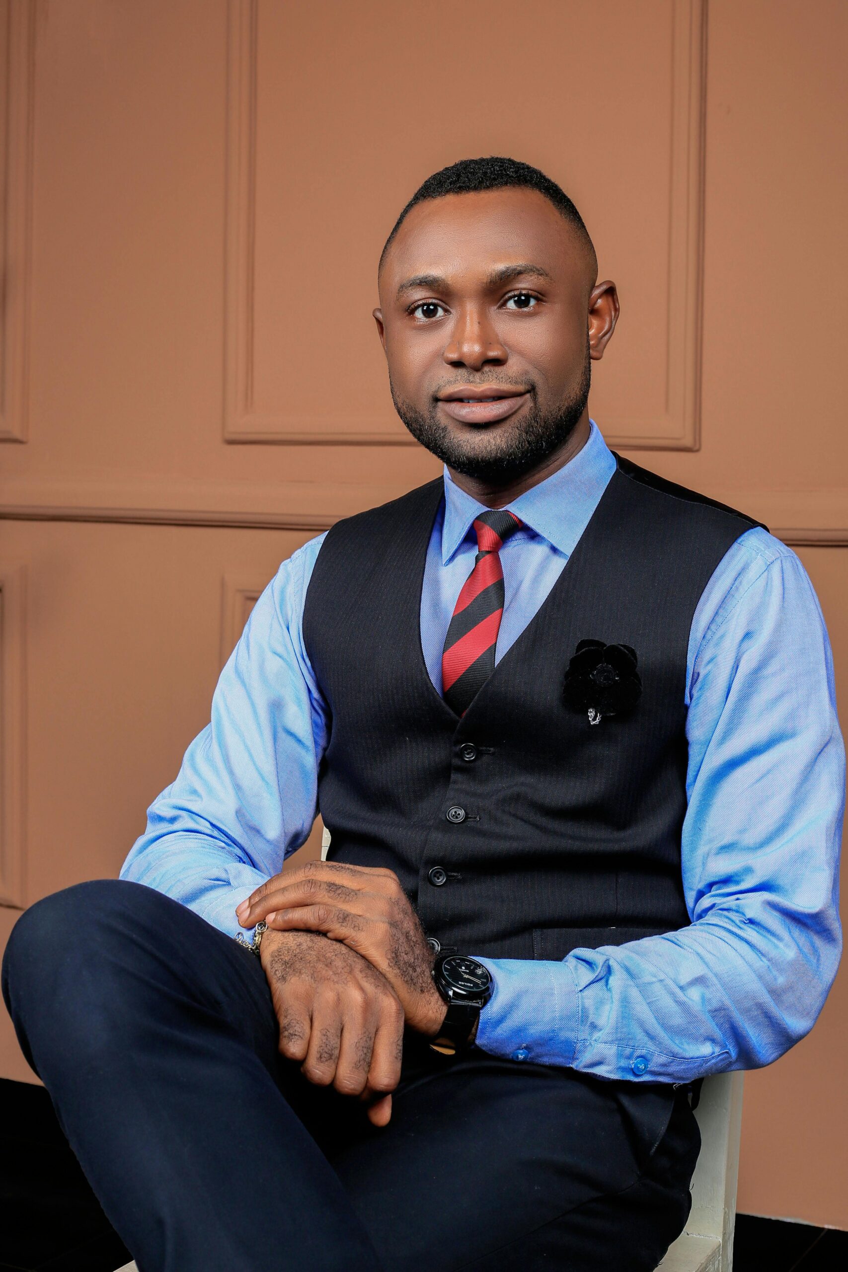 Portrait of a stylish man in a blue shirt and vest, seated indoors.